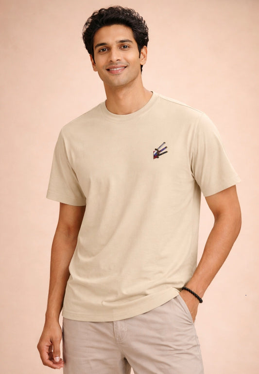 Man wearing a beige t-shirt with a small logo on a beige background