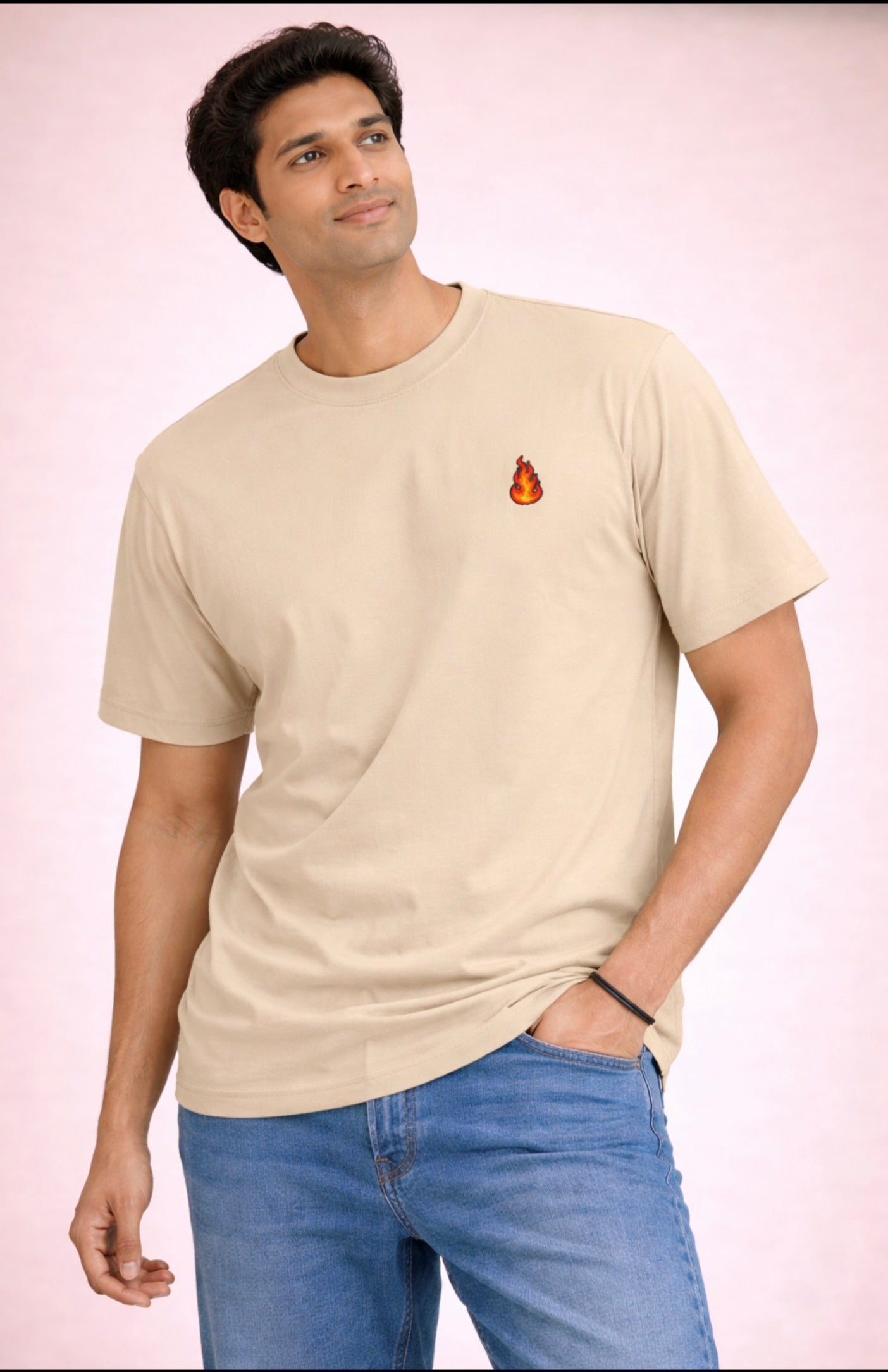 Man wearing a beige t-shirt with a small logo and blue jeans on a light pink background
