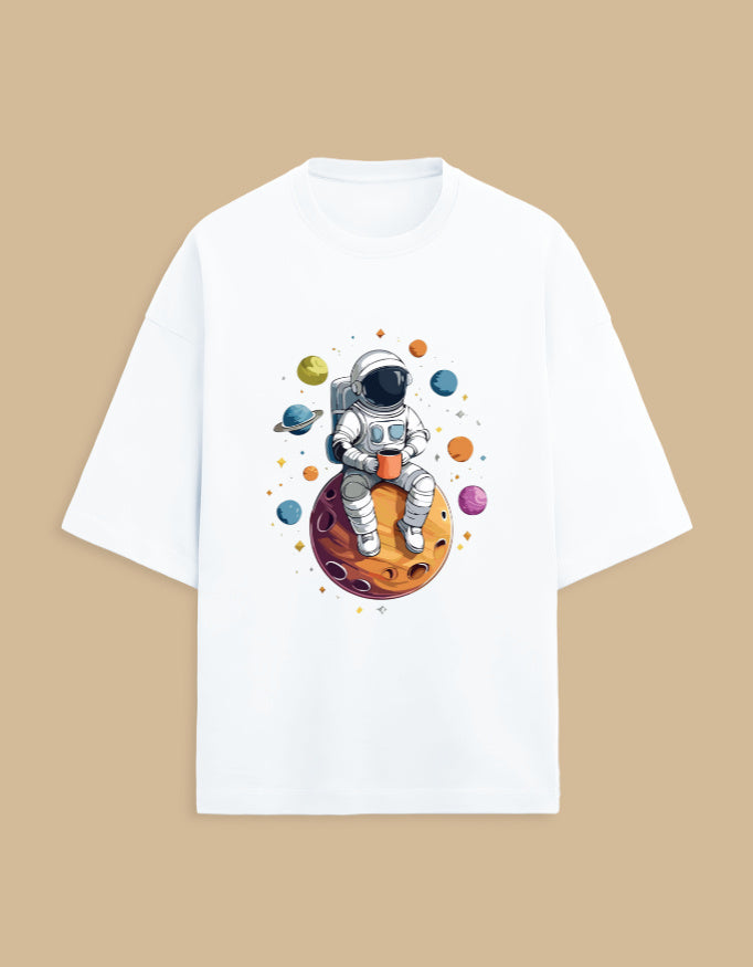 White T-shirt with astronaut holding coffee, sitting on planet, surrounded by colorful planets