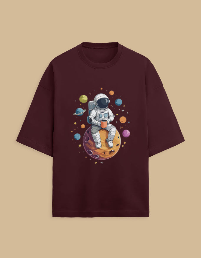 Burgundy t-shirt with astronaut drinking coffee on planet, surrounded by colorful planets