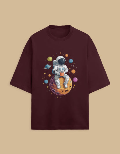 Burgundy t-shirt with astronaut drinking coffee on planet, surrounded by colorful planets
