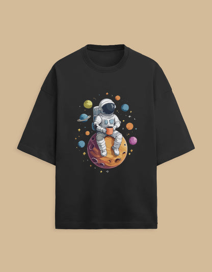 Black t-shirt with astronaut sitting on planet, holding a mug, colorful planets background