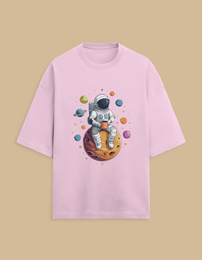 Pink t-shirt with cartoon astronaut holding a mug, sitting on a planet with colorful space design