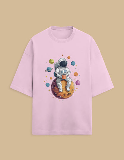 Pink t-shirt with cartoon astronaut holding a mug, sitting on a planet with colorful space design