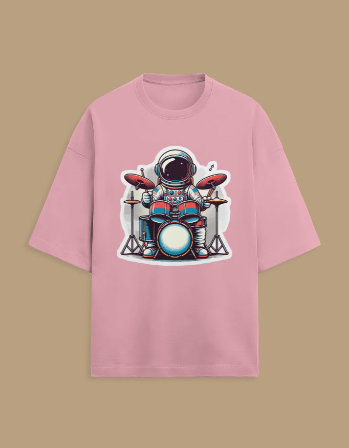 Pink t-shirt with cartoon astronaut playing drums graphic, laid on beige background