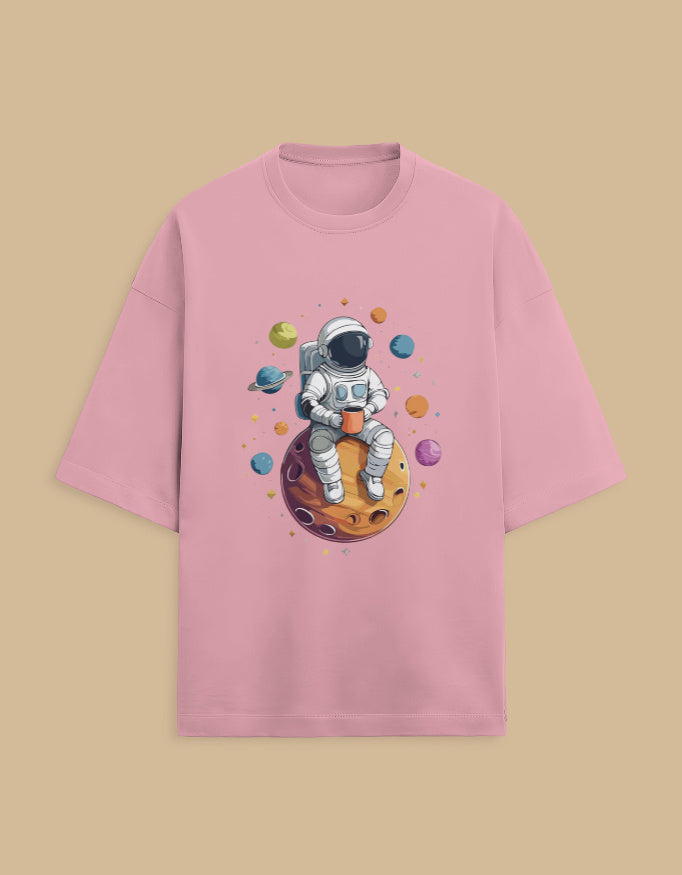 Pink t-shirt with astronaut sitting on planet, holding a cup, surrounded by colorful planets