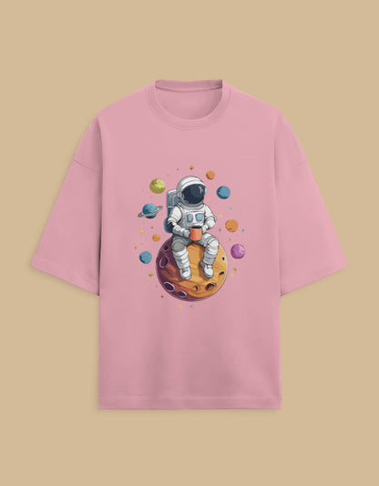 Pink t-shirt with astronaut sitting on planet, holding a cup, surrounded by colorful planets