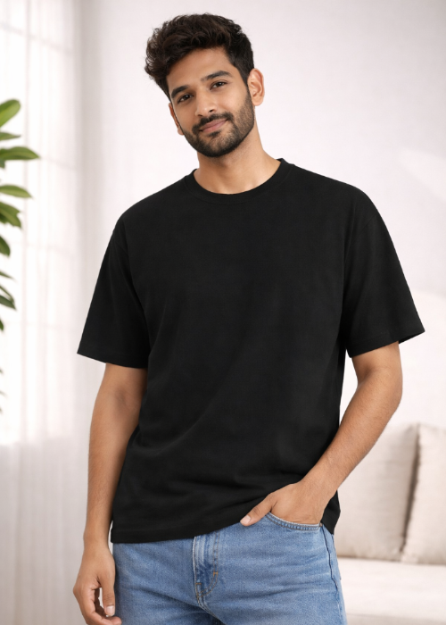 Man wearing a black t-shirt and blue jeans standing indoors with a neutral background