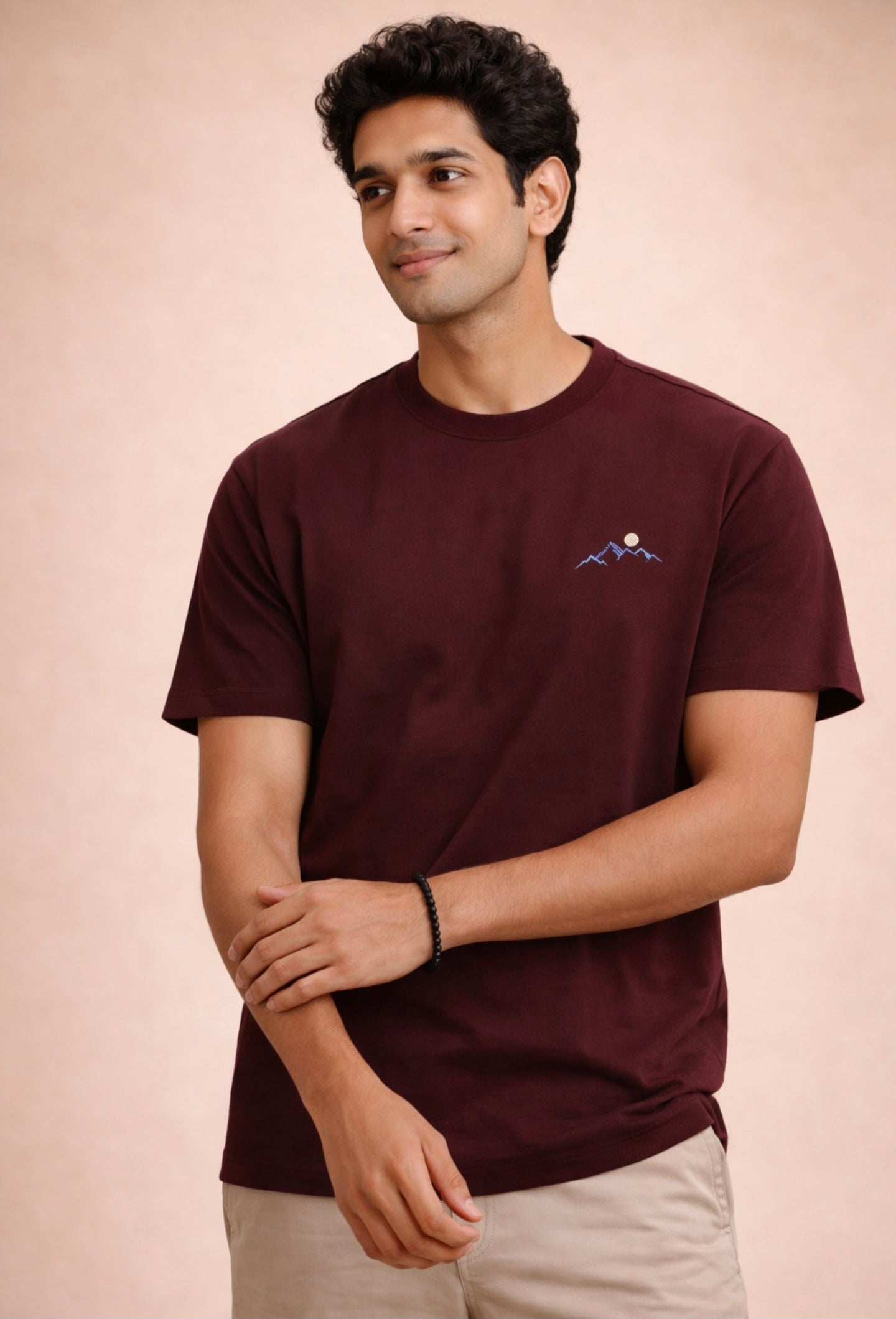 Man wearing a maroon t-shirt with a small logo on a beige background