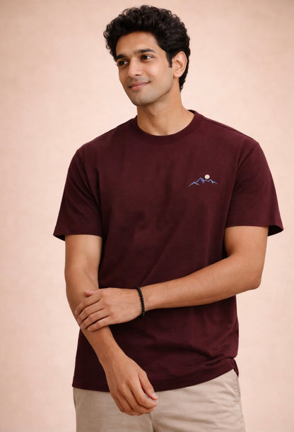 Man wearing a maroon t-shirt with a small logo on a beige background