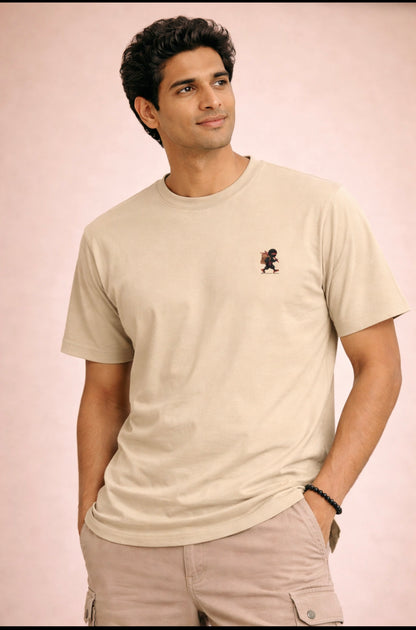 Man wearing a beige t-shirt with a small logo on a light pink background
