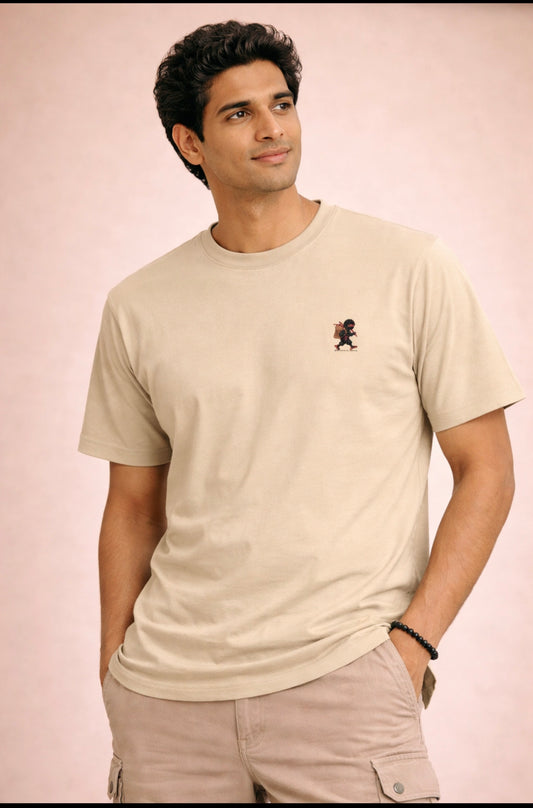 Man wearing a beige t-shirt with a small logo on a light pink background
