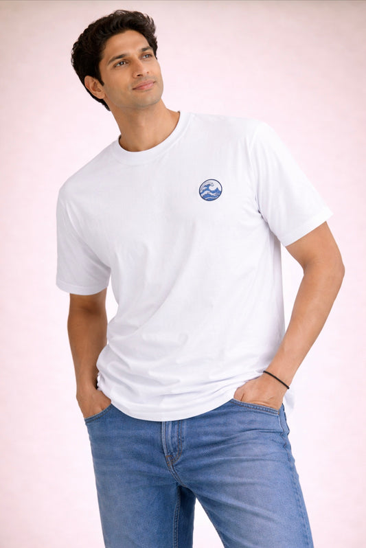 Man wearing a white t-shirt with a logo and blue jeans on a light pink background