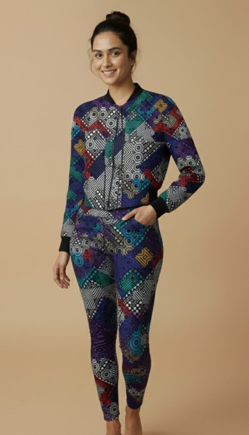 Women's printed activewear co-ord set featuring a colorful geometric bomber jacket and matching leggings, worn by a smiling female model standing barefoot against a beige studio background — iTiDharma athleisure fashion.